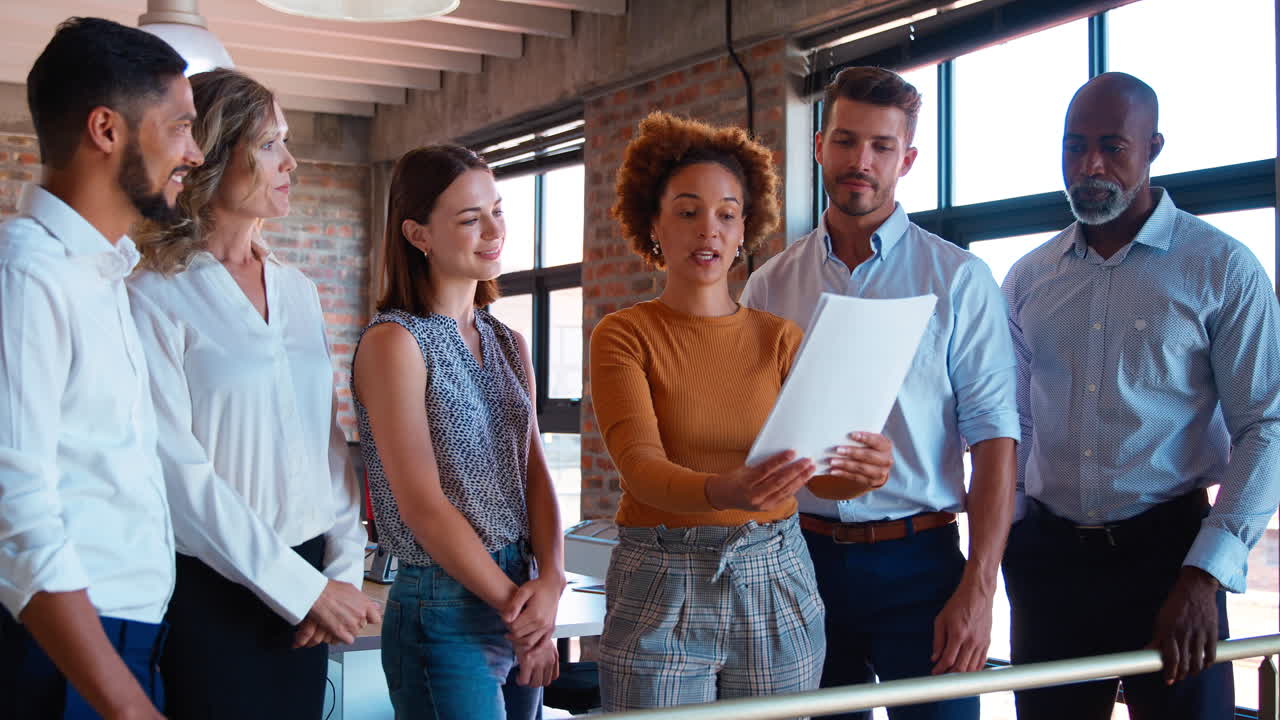 colegas aplaudiendo a una mujer de negocios que lidera una reunión de equipo en una ocupada oficina multicultural