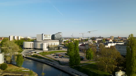 Bydgoszcz-city-skyline---distant-view-of-Nova-Opera,-Brda-river,-and-Zakochanych-bridge---aerial-view