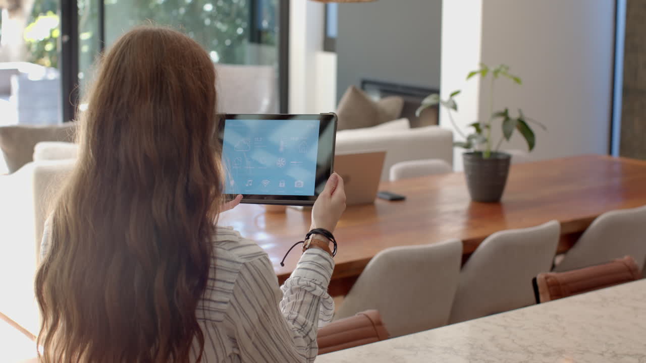 Using tablet, woman standing in modern living room with laptop on table