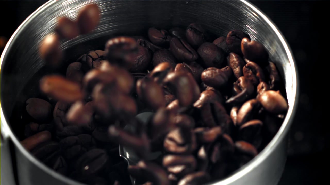 Ristede kaffebønner falder ned i en kaffekværn i slowmotion