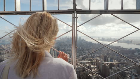 the woman looks at the metropolis below it stands at the fence rear view in the distance visible sky