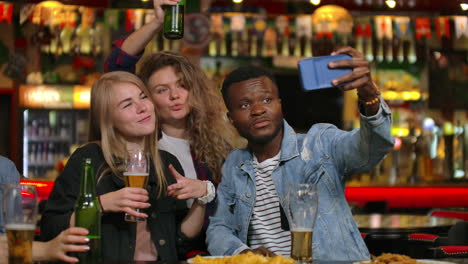 a group of friends multiethnic resting in the bar. friends take a photo on the phone at the bar make a shared photo on the phone. party with friends at the bar with beer.