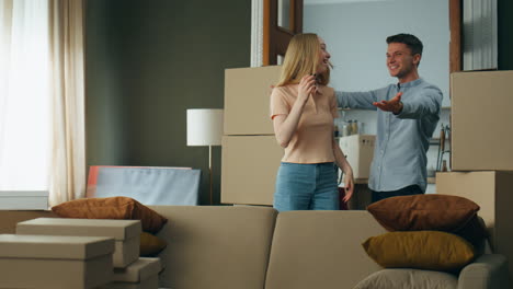 Husband-making-surprise-wife-entering-new-home.-Couple-hugging-near-packed-boxes