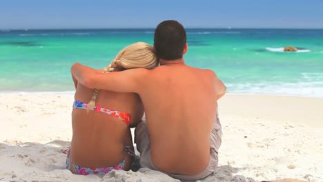 couple sitting on the sand looking at the sea