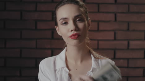 haughty woman looking to camera and showing money stack to camera on brick wall