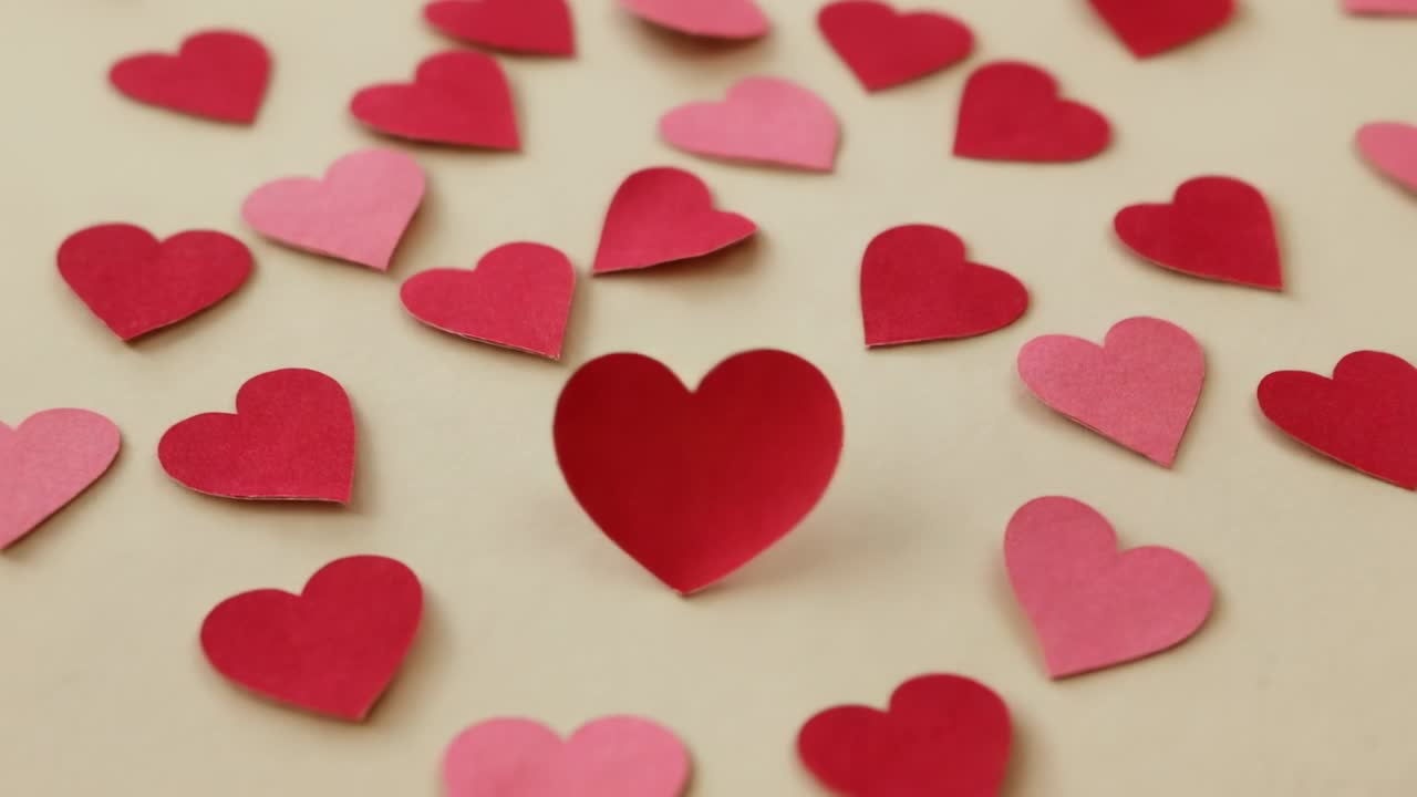 Corações de papel rosa e vermelho caindo e flutuando sobre um livro creme aberto em cima da mesa, formando um denso círculo agrupado