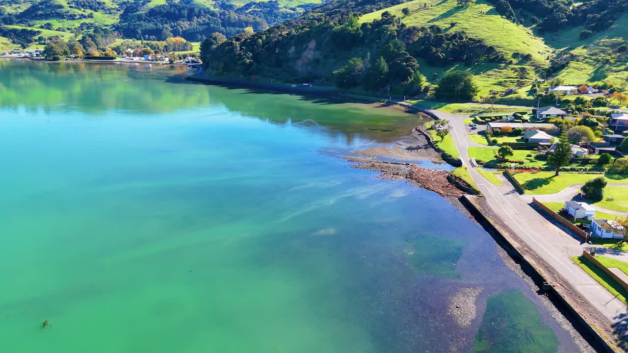 Aerial footage of Akaroa Harbour with vibrant turquoise waters and lush green hills under bright daylight