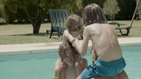 two boys sitting on father and brother's necks and having fun in the swimming pool