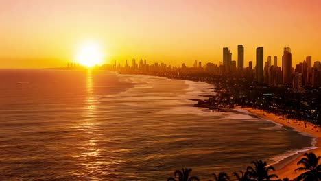 sunset casts a warm glow over a city coastline, with skyscrapers reflecting beautifully on the ocean's surface