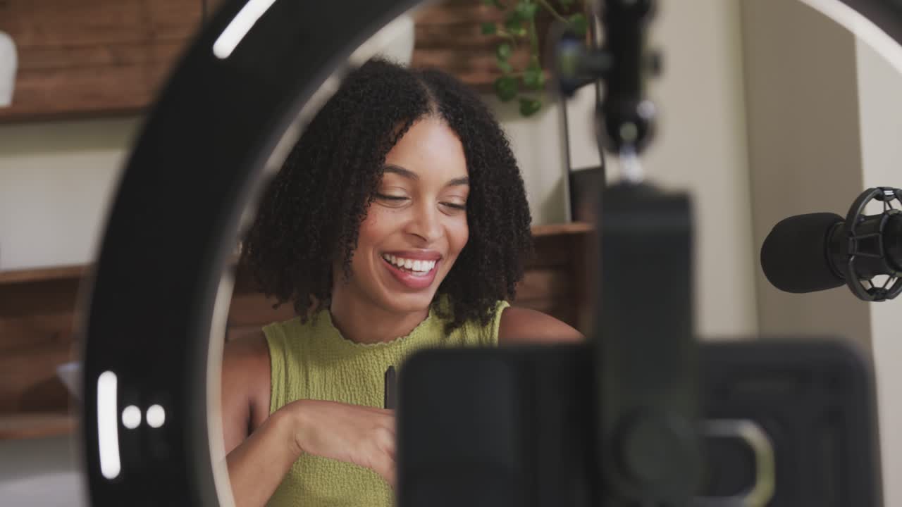 Woman starting cell recording under ringlight for vlog talking reading notes leaning to mic at home