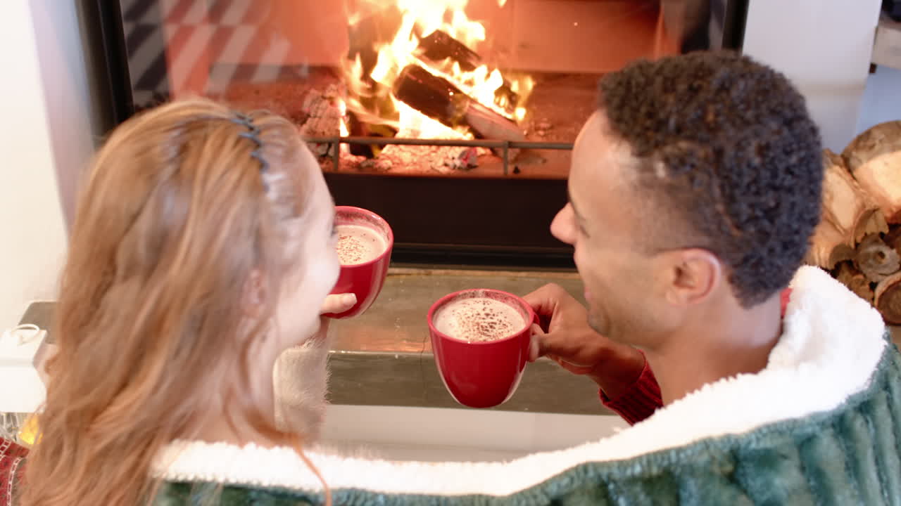 Couple enjoying hot cocoa by cozy fireplace during Christmas at home