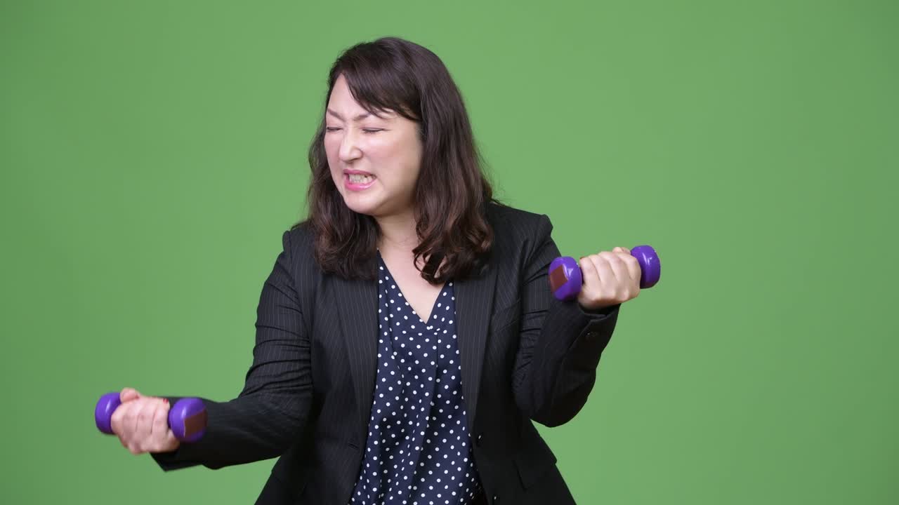 Mature beautiful Asian businesswoman exercising with dumbbells