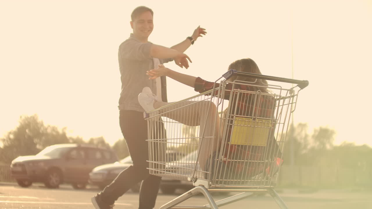 vista lateral de un joven y una mujer divirtiéndose al aire libre en carros de compras. jóvenes multiétnicos compitiendo en carros de compra. en la zona de estacionamiento con sus