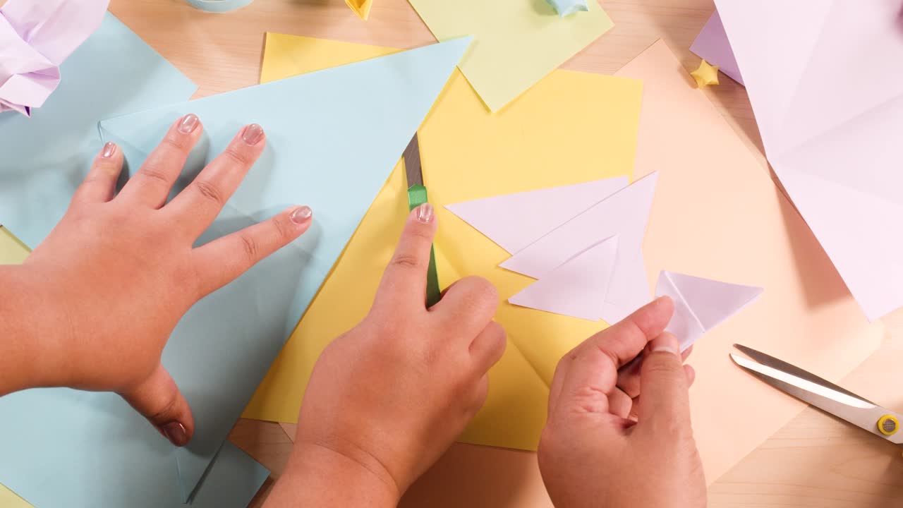 Vista dall'alto di mani che piegano e tagliano carta colorata per un progetto di creazione origami