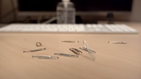 een hand vol paperclips die langzaam in super slow motion beetje bij beetje op een bureau vallen