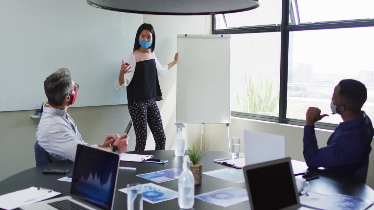 mujer asiática con máscara facial dando una presentación a sus colegas en la sala de reuniones en una oficina moderna