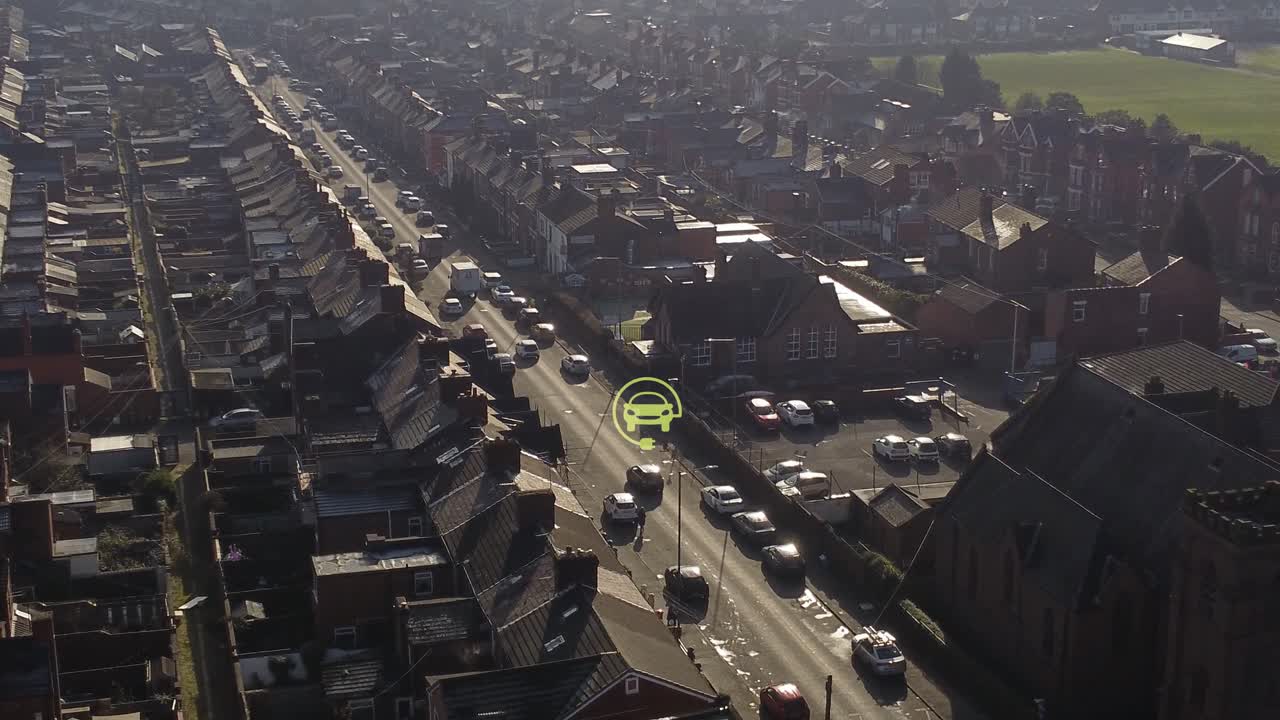 vista aérea del símbolo cargado de un coche eléctrico en órbita que parpadea sobre el vehículo que conduce un largo camino en el barrio británico al amanecer.
