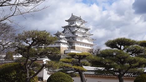 majestic himeji castle in hyogo, japan framed by pine trees and stone walls under a dramatic cloudy sky