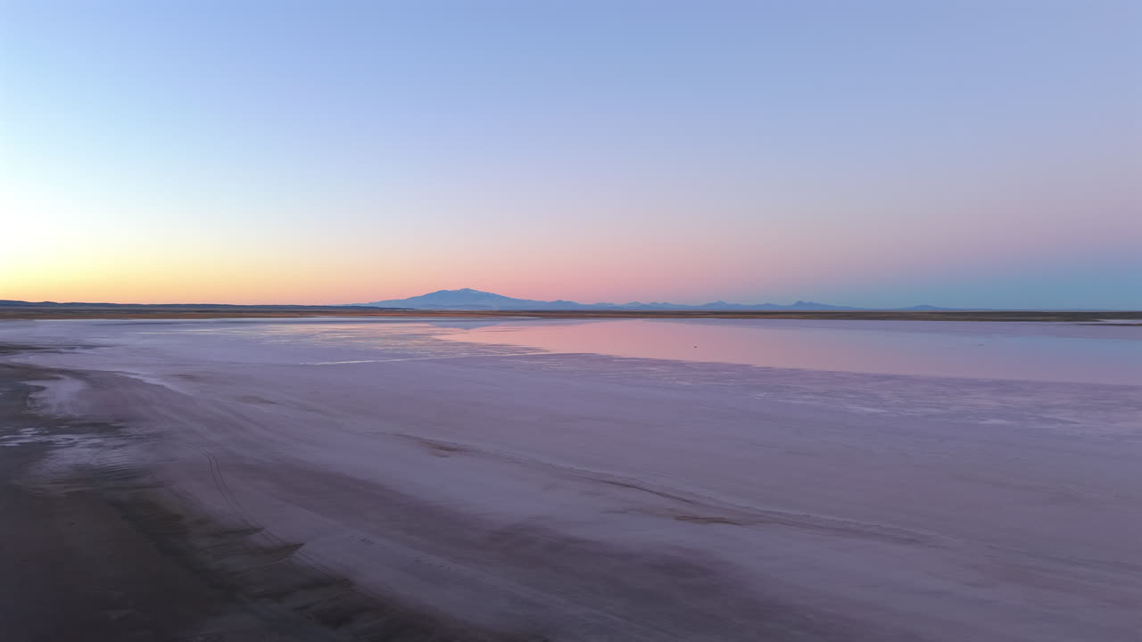 Aerial movement along the flat salt lake shoreline of Salinas del Diamante national protected area at sunset, Mendoza, Argentina.