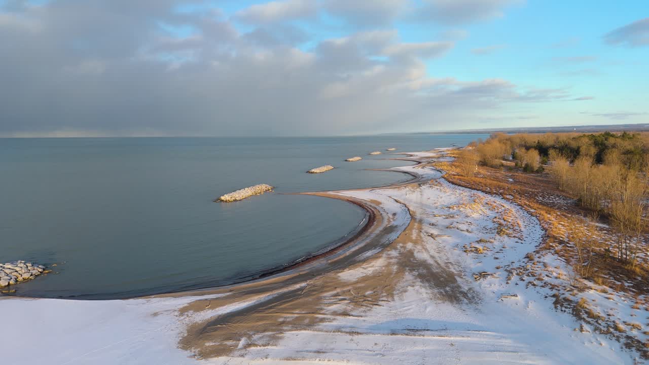 Aerial shot pushing in on a snow covered Presque Isle Beach at golden hour with a storm approaching