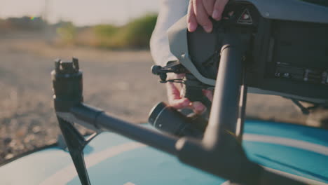 A-person-putting-a-camera-on-a-drone-with-plants-and-the-sky-in-the-background