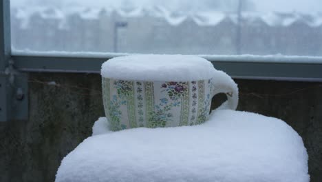 a tea cup flower pot is covered with snow during a snowstorm in winter