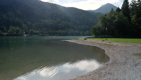 static wide shot of clear achensee lake in austria during sun is rising up behind the mountain hills in summer