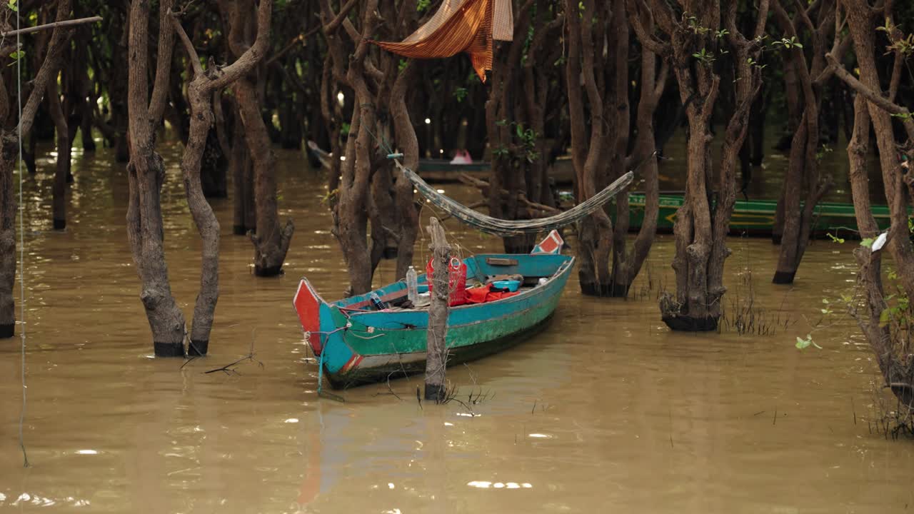 A small wooden boat rests between flooded trees in a Tonle Sap floating village, Cambodia