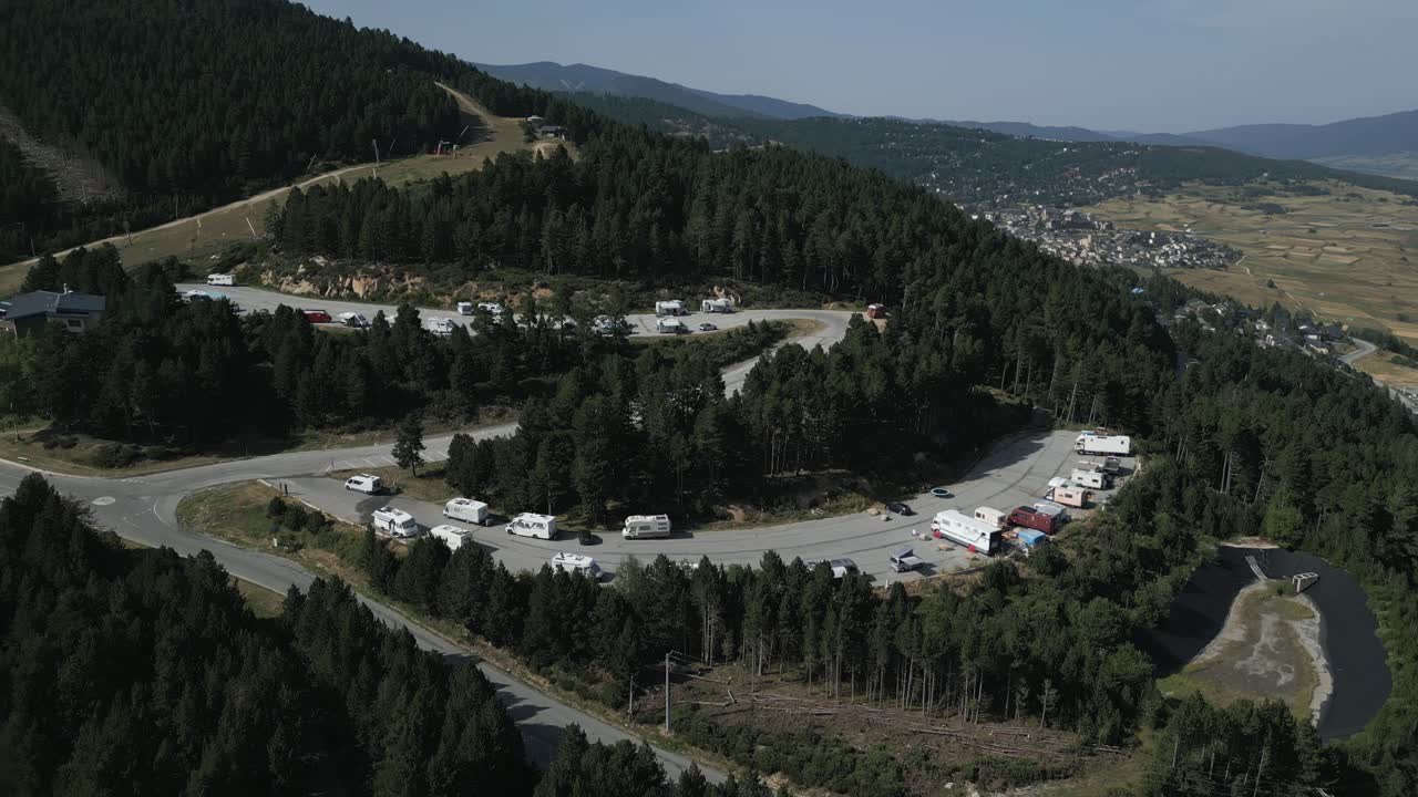 Un'ampia ripresa aerea mostra una pittoresca area di sosta per camper e furgoni immersa tra le montagne boscose di Les Angles, in Francia, con vista sulla valle sottostante