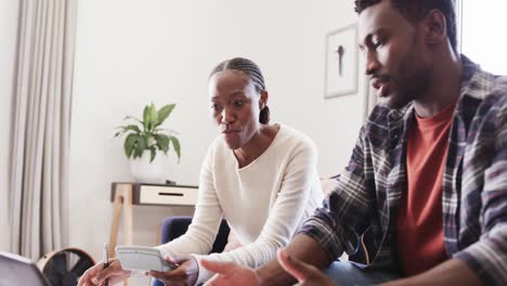 serious african american couple using calculator and laptop discussing finance at home, slow motion