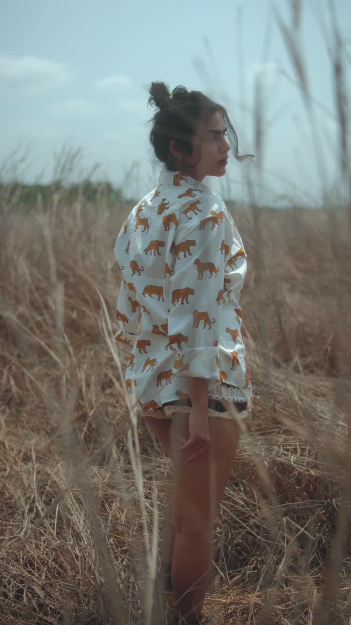 Young woman in a lion-print shirt, standing in a dry field, looking back confidently