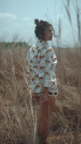 young woman in a lion-print shirt, standing in a dry field, looking back confidently