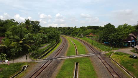 Aerial-flyover-rails-with-railroad-crossing-in-tropical-area-during-sunny-day,-Indonesia