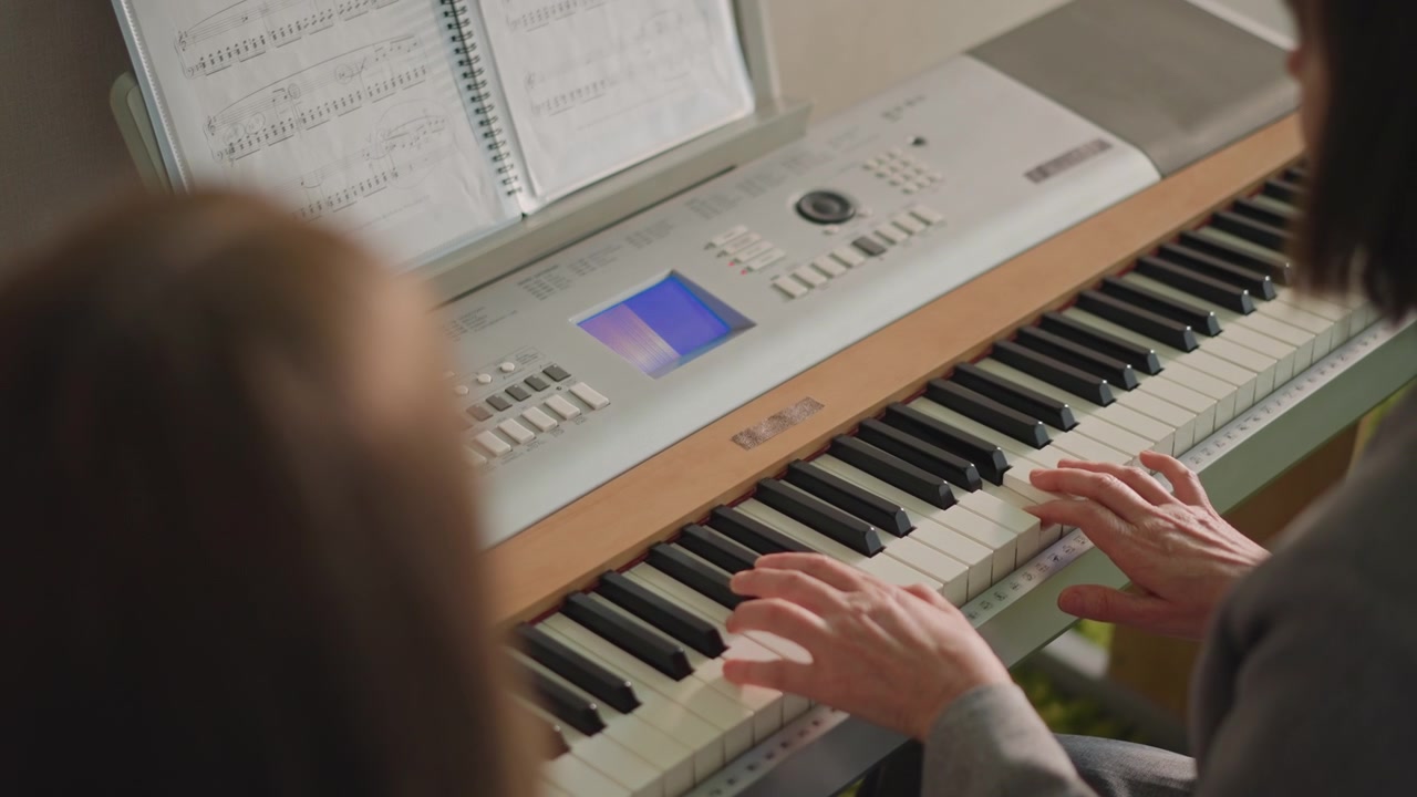 Il tutor assiste al pianoforte. L'insegnante aiuta con la tecnica pianistica. L'istruttore di musica guida le mani durante la sessione di pratica del pianoforte. L'insegnante esperto fornisce una guida mirata allo studente sulle competenze pianistiche.