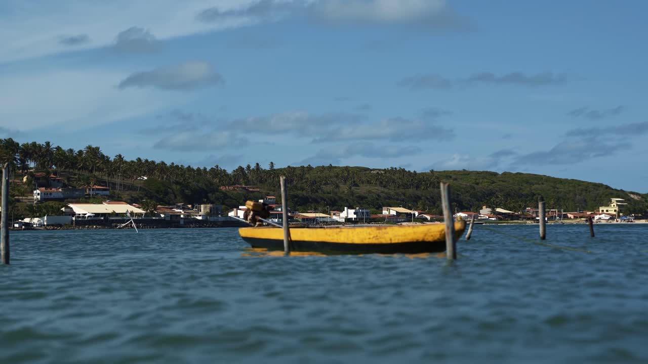 브라질 리오그란데두노르테 주 칸구아레타마의 바라 데 쿤하우 해변 근처에서 빠르게 움직이는 열대 브라질 강에 있는 나무 기둥에 묶인 작은 노란색 모터보트