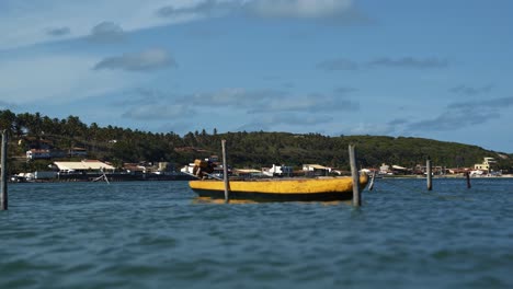 Ein-Kleines-Gelbes-Motorboot,-Das-An-Einem-Holzpfosten-In-Einem-Großen,-Schnell-Fließenden-Tropischen-Brasilianischen-Fluss-In-Der-Nähe-Des-Strandes-Barra-De-Cunhau-In-Canguaretama-Im-Bundesstaat-Rio-Grande-Do-Norte,-Brasilien,-Festgebunden-Ist