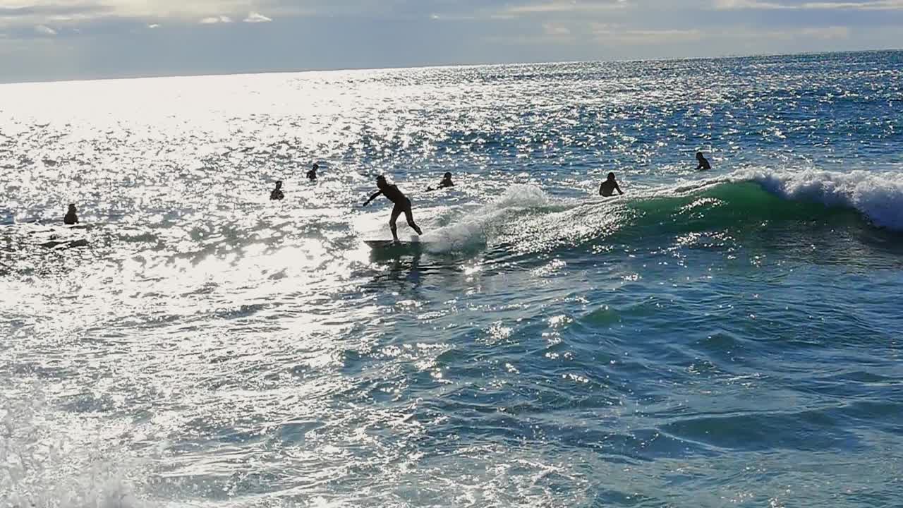 Slow motion (120fps): male surfer surfing the wave among a lot of surfers and stopping to avoid crashing into a stone sea barrier in Barcelona, Spain