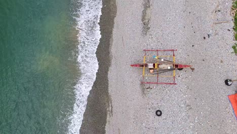 traditional filipino banka boat rests on a pebbled beach by calm turquoise waters from above
