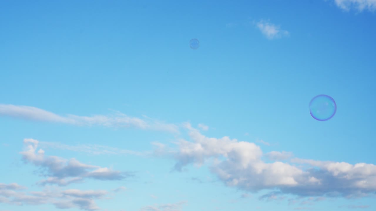Soap bubbles slowly fly against blue sky. Floating bubbles under sky with white clouds. Childhood, outdoor activities and games on sunny warm day