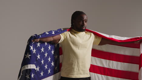 studio portrait shot of man wrapped in american flag celebrating 4th july independence day