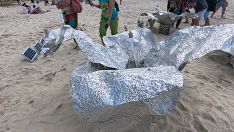 people interacting with metallic sculptures on the beach