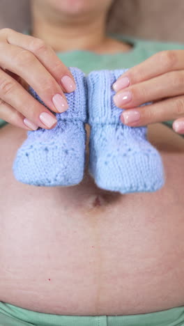 belly of a pregnant girl. future mother playing with knitted baby socks on her bare stomach. concept of health during pregnancy. close-up. vertical video