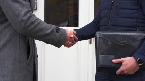 two businessmen shaking hands with document binder in front of the door