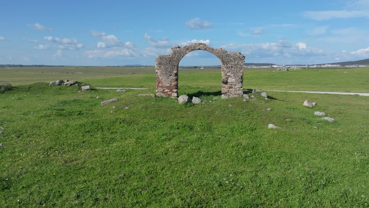 Frontal drone shot over green pastures approaching the “Puerta de Arenas,” an old stone and brick archway. The drone skims closely over the top, creating a dynamic and immersive perspective.