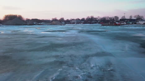 flying shot over the icy lake revealing a stone quarry, a pier and some boats