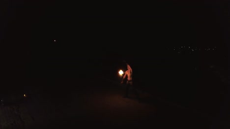 joven hombre rubio hace trucos con el fuego gira dos antorchas ardientes por la noche en el fondo negro de la ciudad viajando