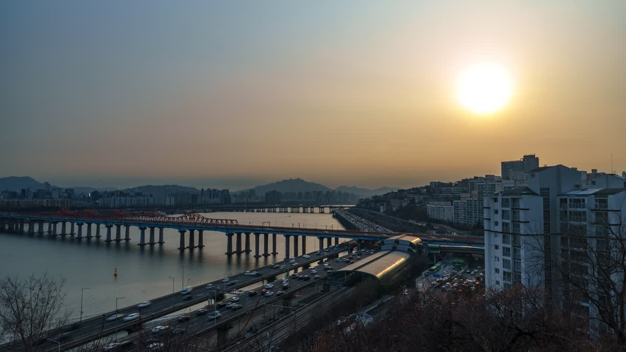 Time-lapse di Seoul, Corea del Sud, traffico sulla superstrada Gangbyeonbuk-ro, Ponte Donho, Stazione di Oksu, Fiume Han che riflette un tramonto dorato, montagne in silhouette, foschia invernale, cielo arancione drammatico