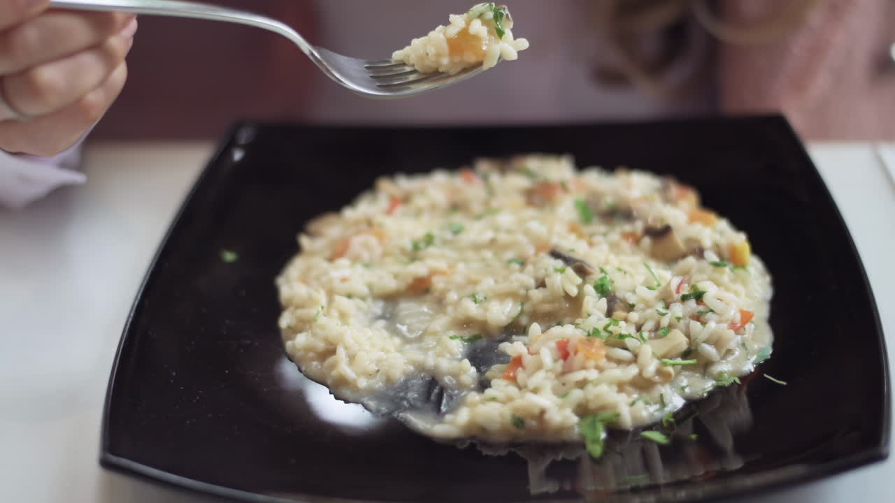 Close up of a woman eating risotto from a black plate at a restaurant