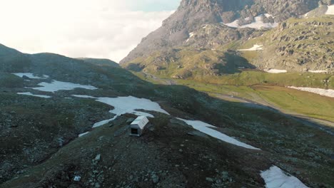 aerial: flying around mountain hut in alpine valley at sunrise