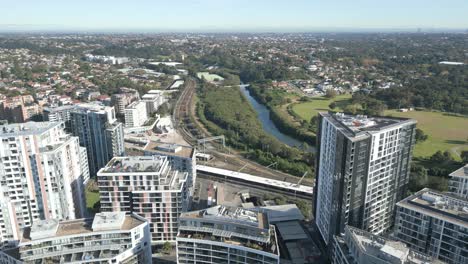 aerial shot flying forward among the residential apartments in sydney suburb with tall buildings, train lines, and park in the background, beautiful summer day with bright green trees and grass